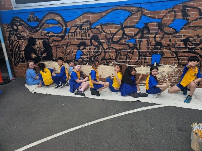 Students adding base colours to the Bexley Public School mural during the early stages of the “Our Living Country” project