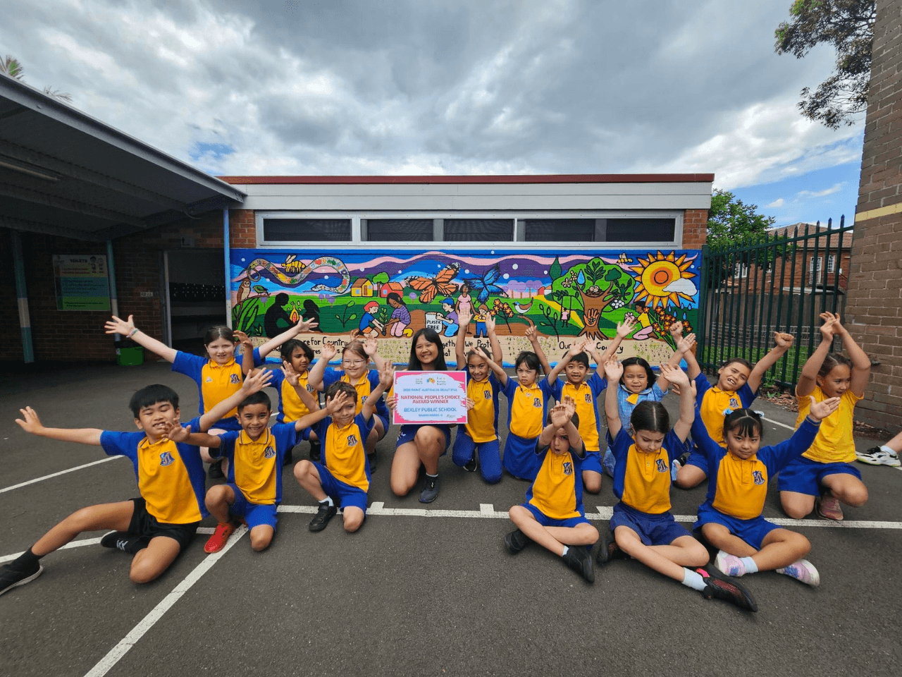 Students celebrating in front of the completed Bexley Public School mural, “Our Living Country”, after winning Paint Australia Beautiful